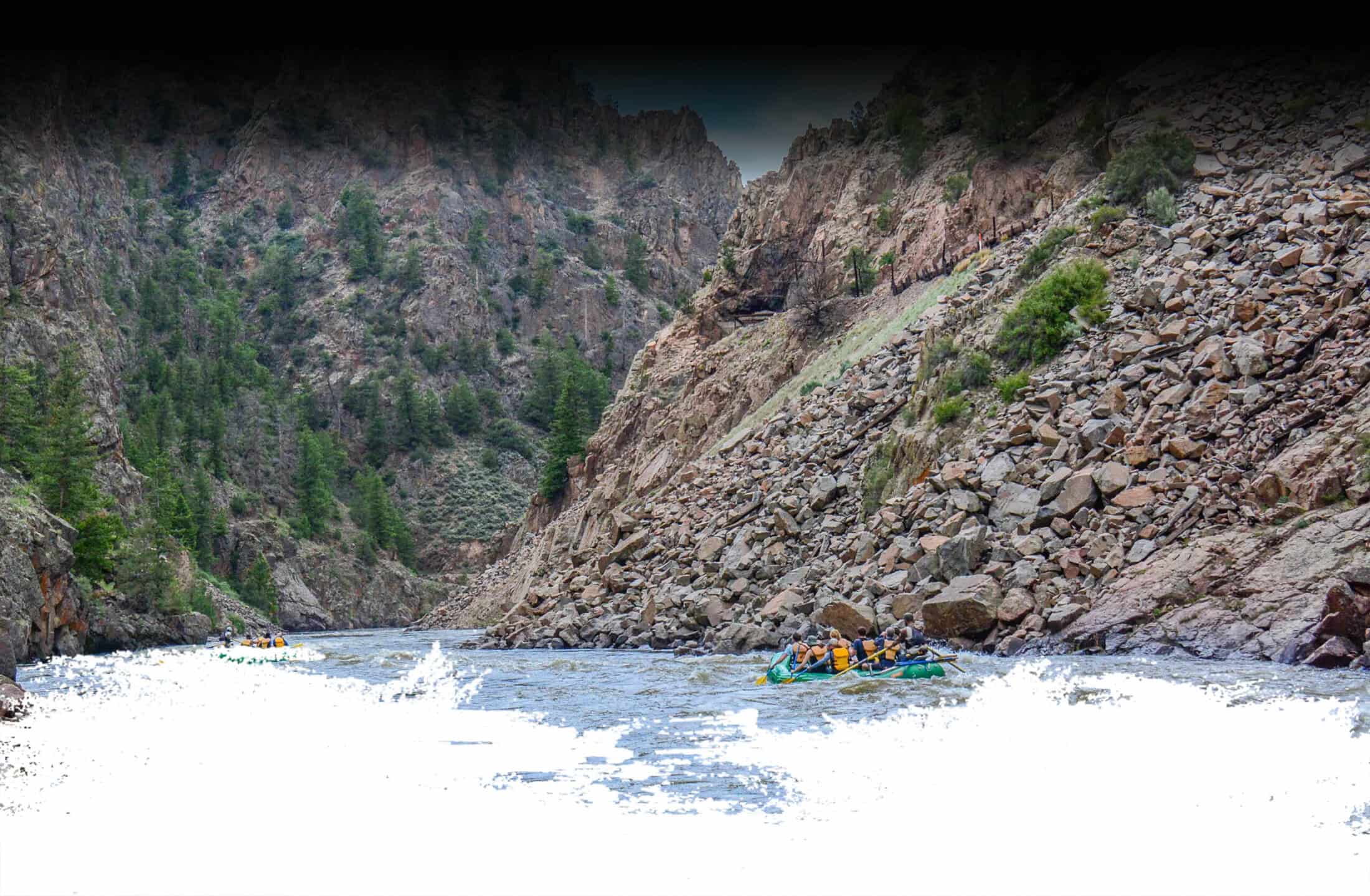 Adventurous group of rafters paddling through churning rapids on white water rafting Steamboat Springs offers with mountain scenery surrounding the river canyon.